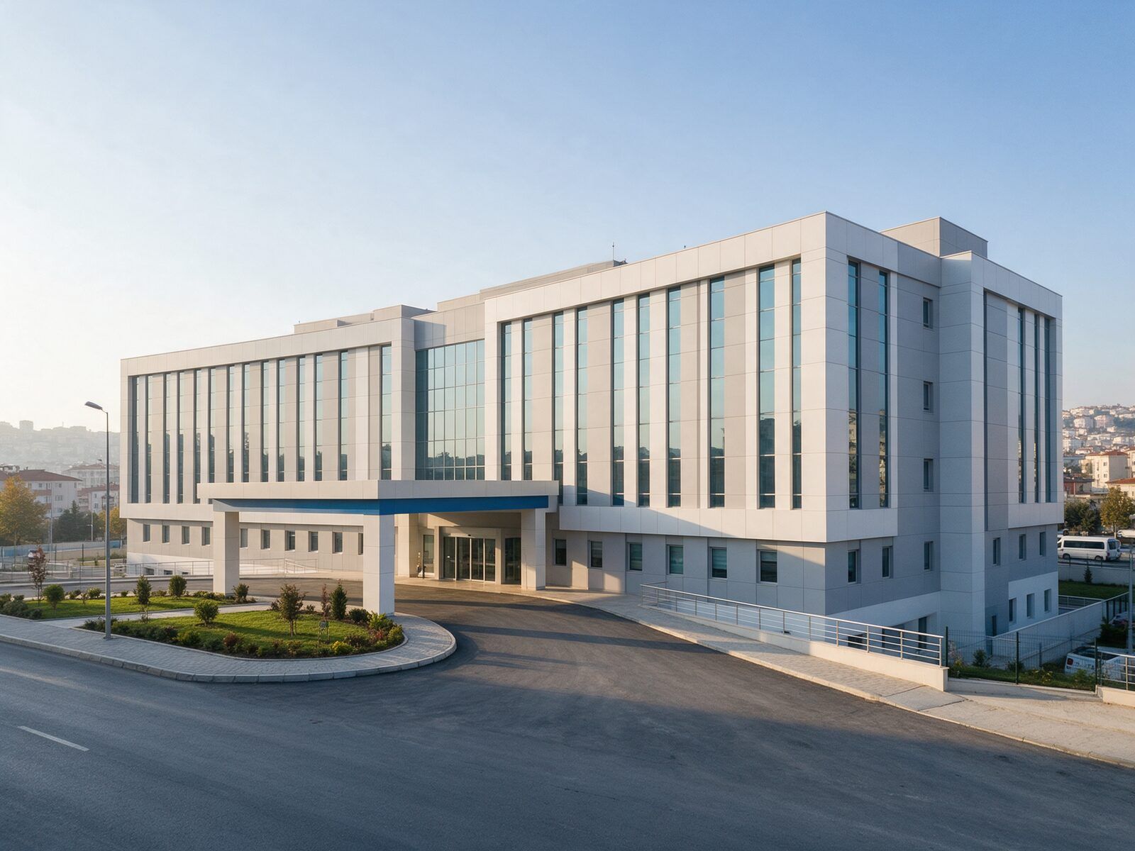 Hastanenin dış cephesi: açık gri ve beyaz bina, mavi şeritli giriş saçağı